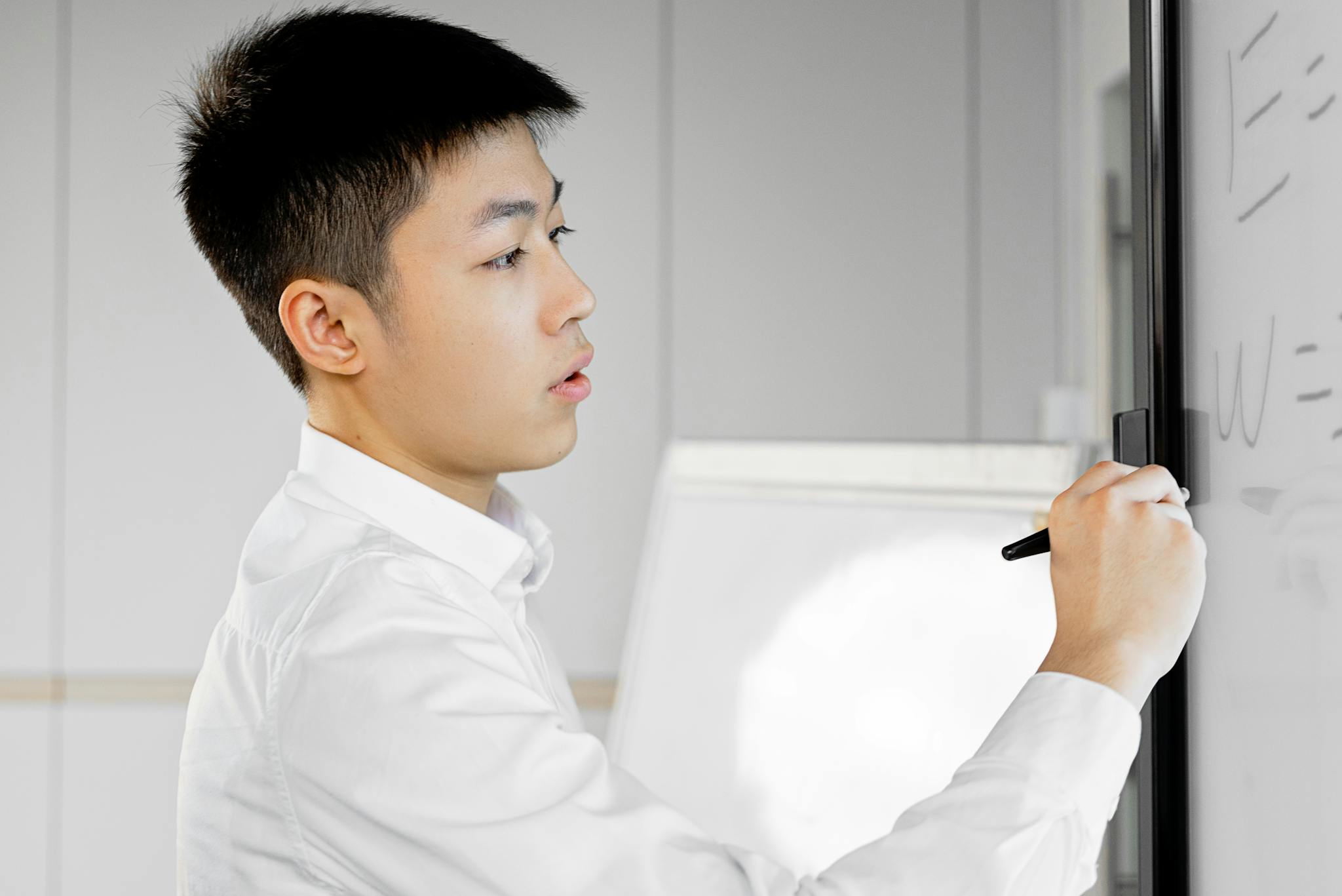 Young Asian professional writing with stylus pen on interactive board during office presentation.